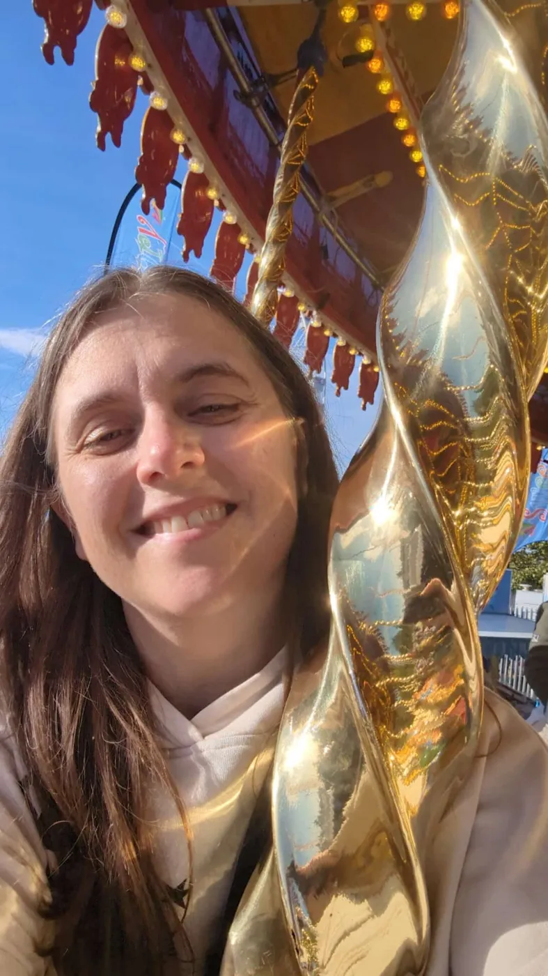 Liz grinning beside the gold twisted pole of a fairground carousel at Hull Fair