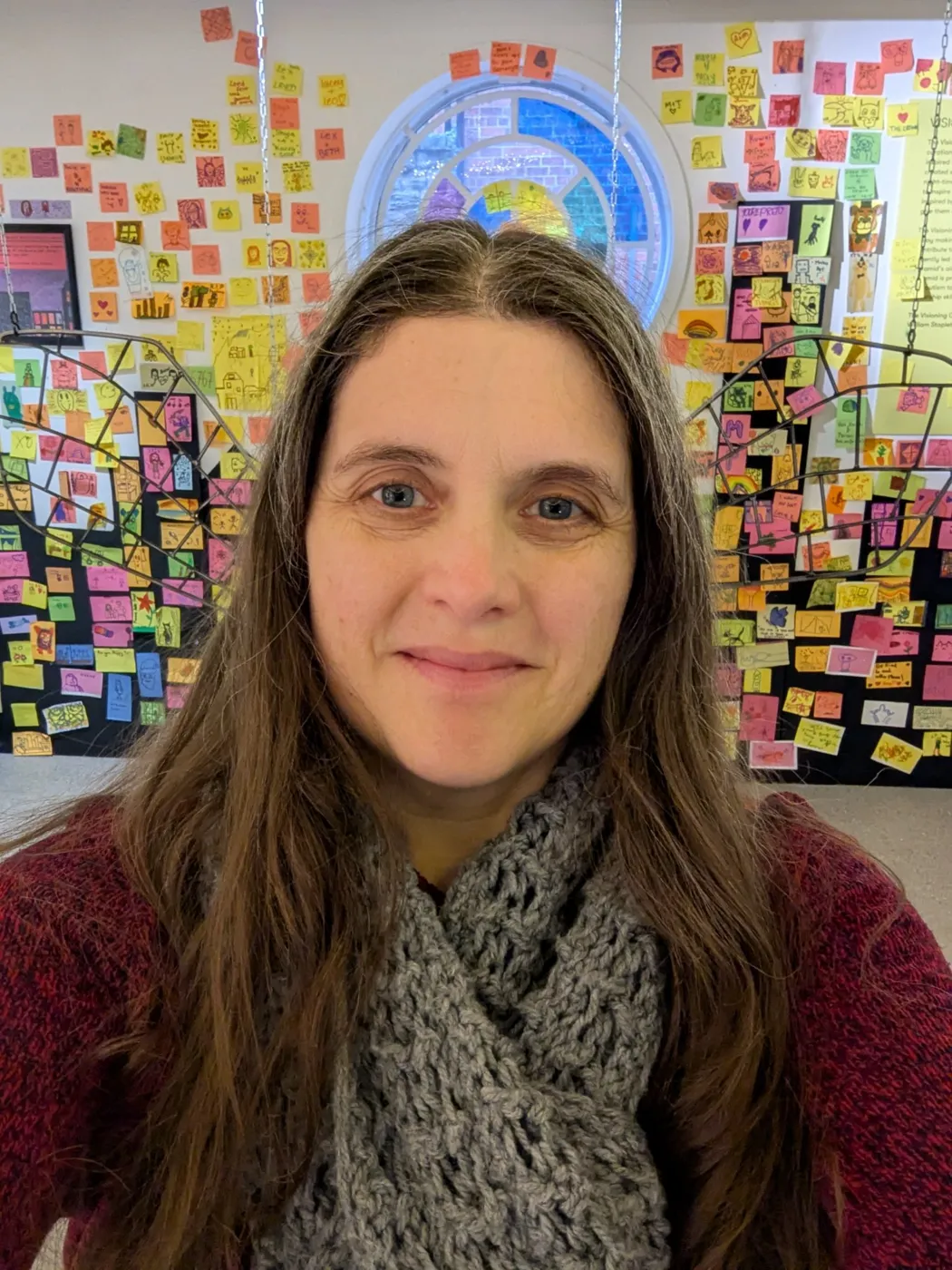 Liz in front of a gallery wall covered in colourful post-it note art