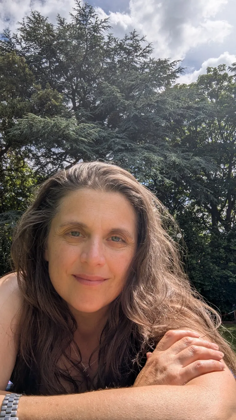Liz, coach at Be More Coaching, smiling warmly in a garden under tall trees