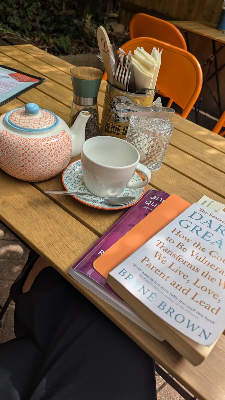 A teapot, cup and coaching books including Daring Greatly by Brené Brown on a cafe table during a session